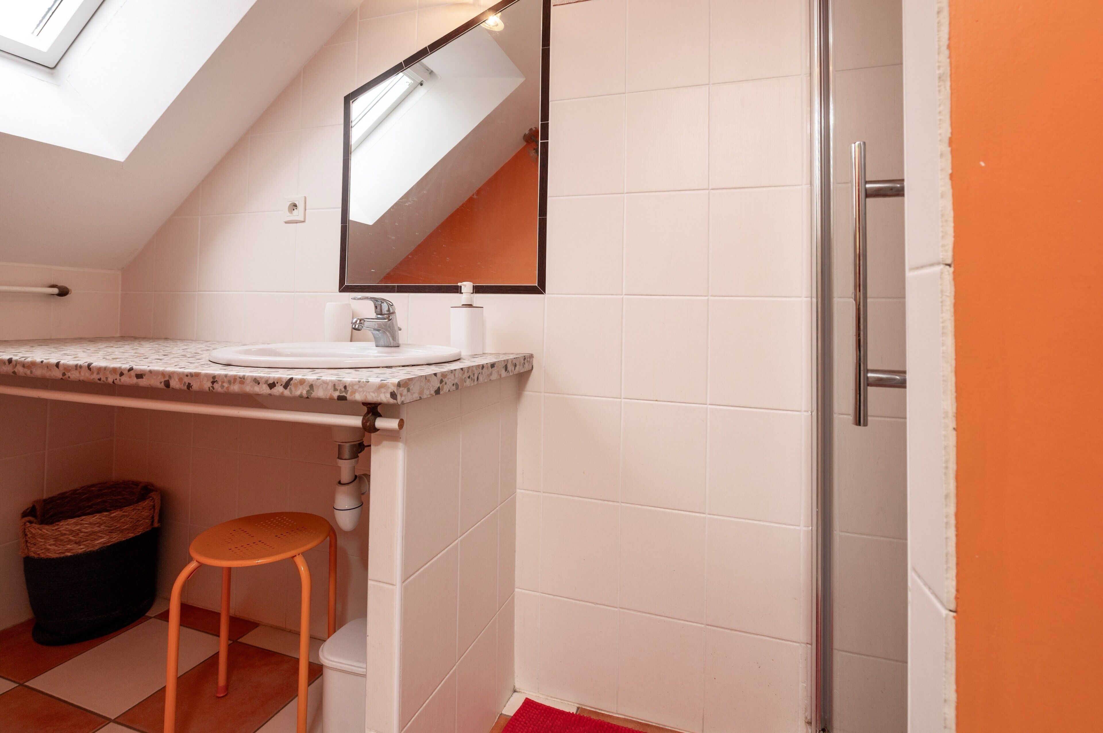 Ein Badezimmer mit Dachfenster, Waschbecken, Spiegel, Toilette und Dusche.