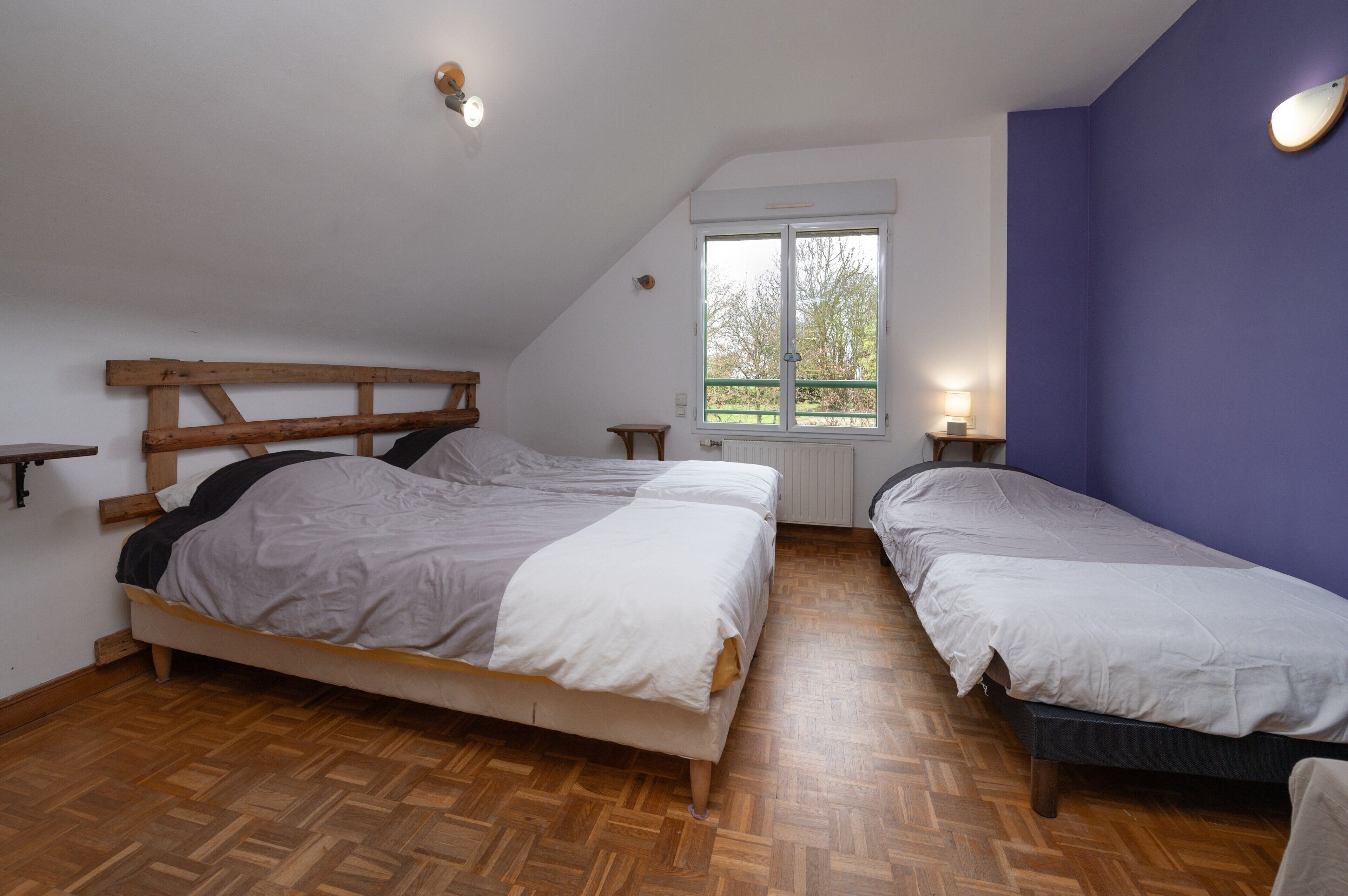 Ein Schlafzimmer mit zwei Betten, Holz-Kopfteilen, einem Fenster mit Blick und einem kleinen Nachttisch mit Lampe.