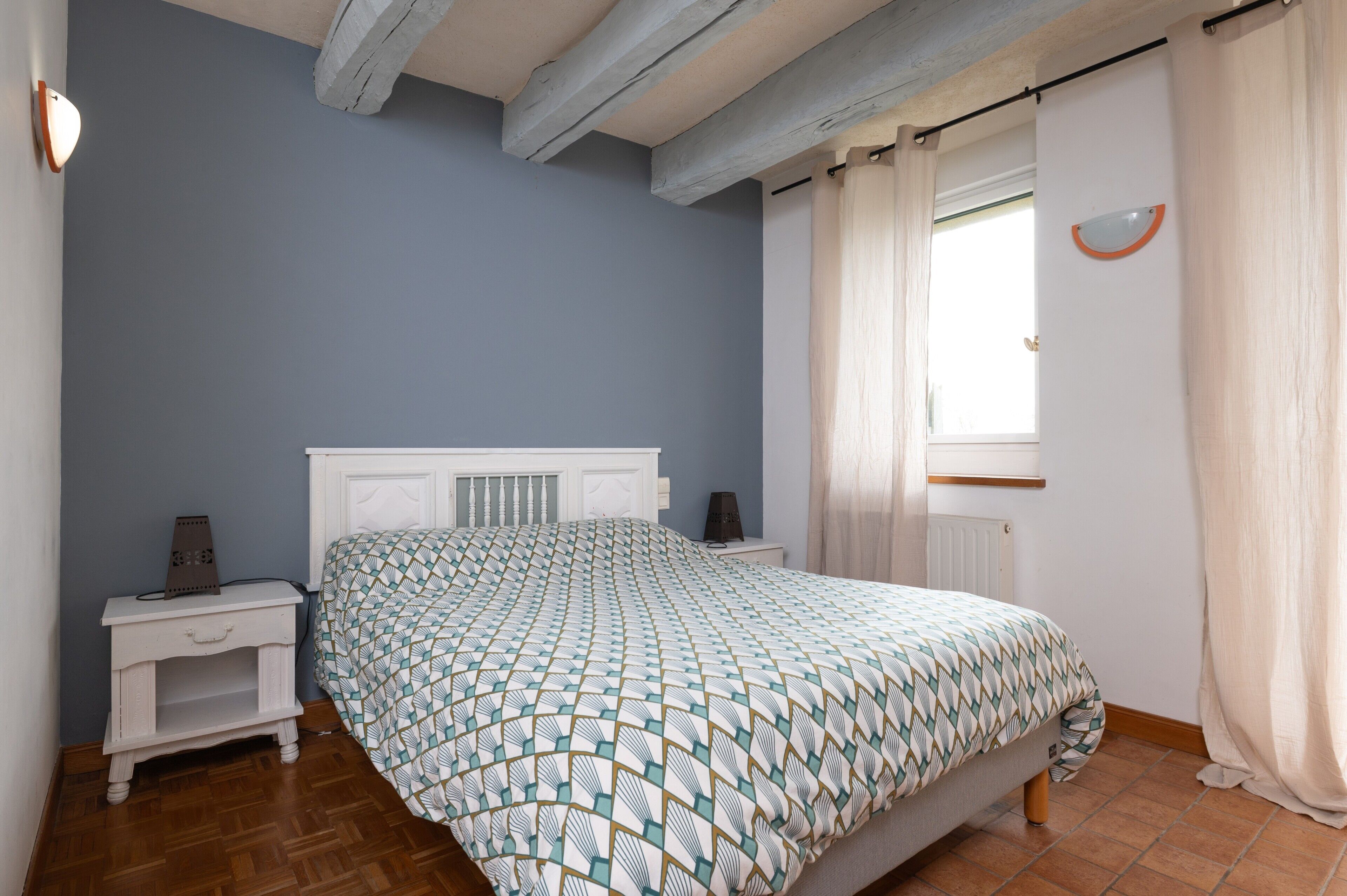Une chambre à coucher avec un lit, une table de chevet et une fenêtre avec des rideaux.