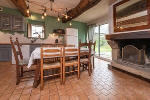 Ein Essbereich mit Holztisch und Stühlen, eine Küche mit Kühlschrank und ein Kamin.