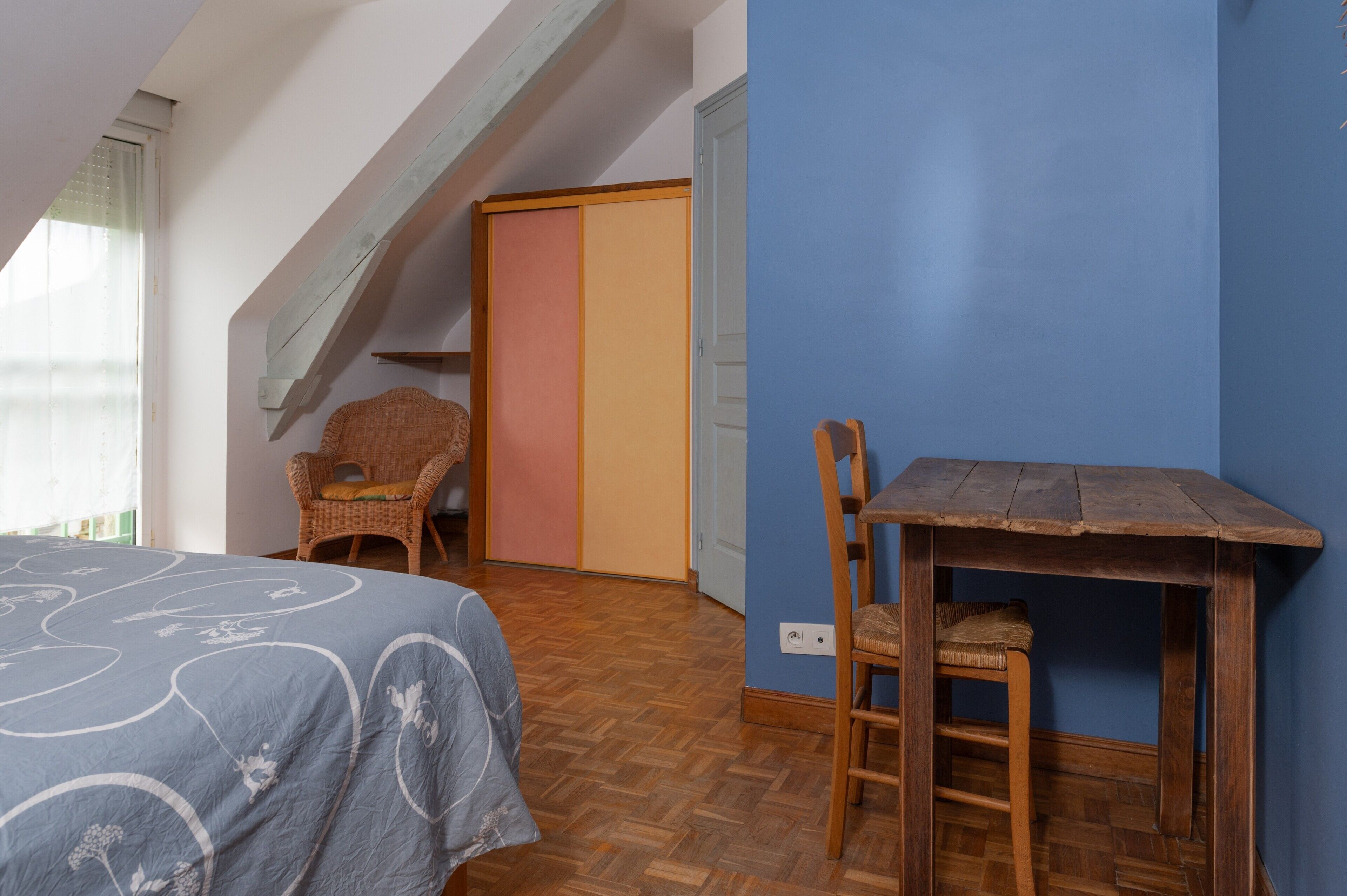 A room with a bed, a chair, a small table, a wardrobe, and a sloped ceiling.