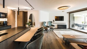 A modern kitchen with a built-in microwave, a dining area with a long wooden table and cushioned chairs, and a large window offering a view of the outdoors. - Apartment 'Les Ovis Comisana' – Opening May 2026 with Private Jacuzzi (San Leonardo in Passiria)