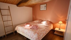 Ein Schlafzimmer mit einer Holzlade, einem Bett mit floralem Bettzeug, einer Nachttischlampe und einem gerahmten Bild an der Wand.
