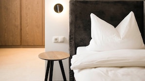 Ein Schlafzimmer mit einem Bett, einem runden Holztisch, einer Wandleuchte und einem Holzschrank.
