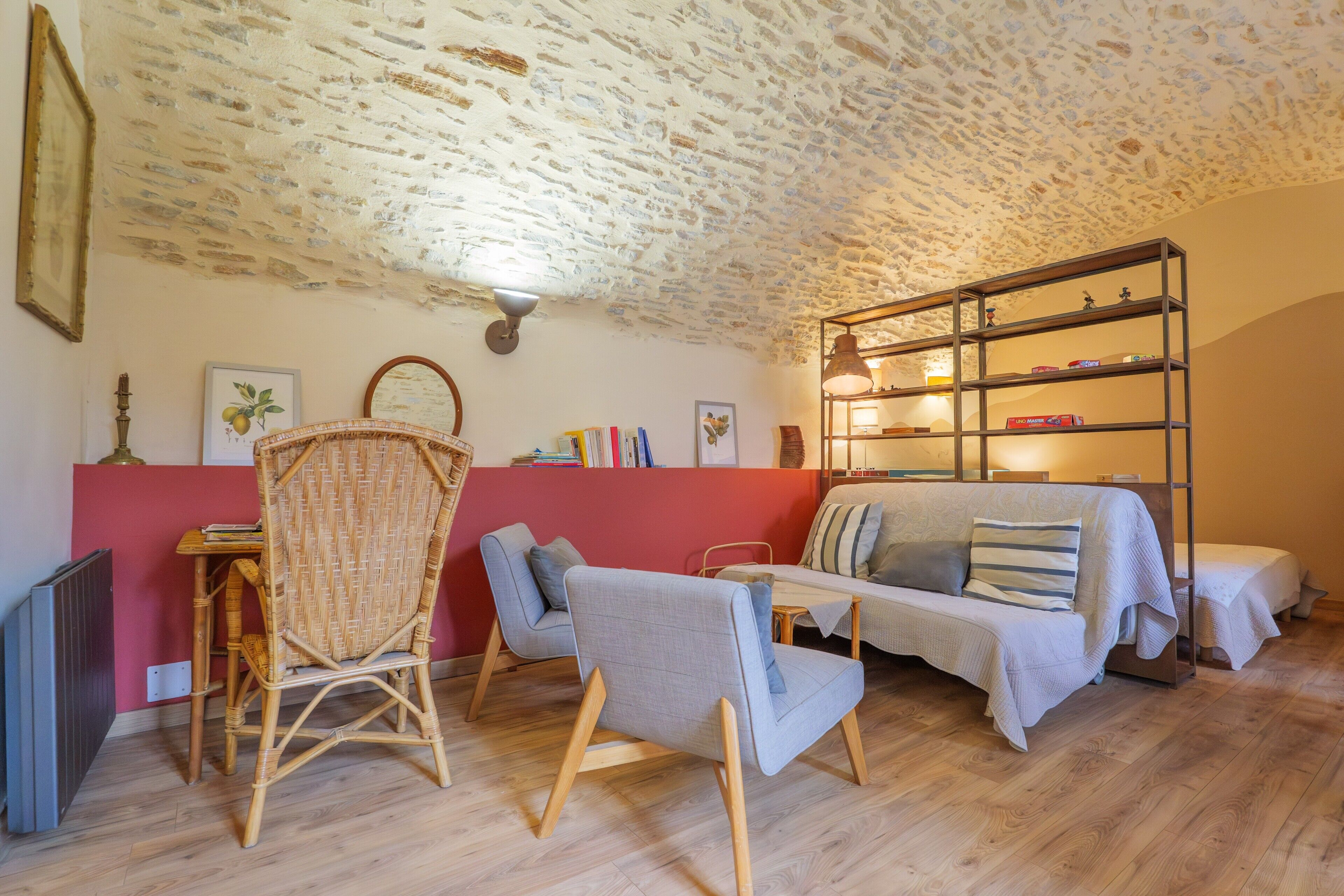 A cozy room with a stone ceiling, a red accent wall, a sofa, a bookshelf, and a wicker chair.