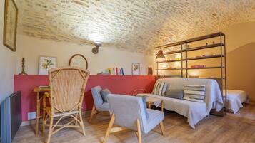 A cozy room with a stone ceiling, a red accent wall, a sofa, a bookshelf, and a wicker chair.