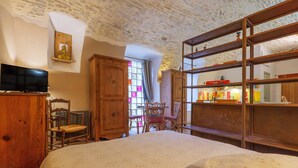 Ein Schlafzimmer mit Bett, Holzmöbeln, einem Fernseher, einem Fenster mit Vorhängen und einem Regal mit Gegenständen.