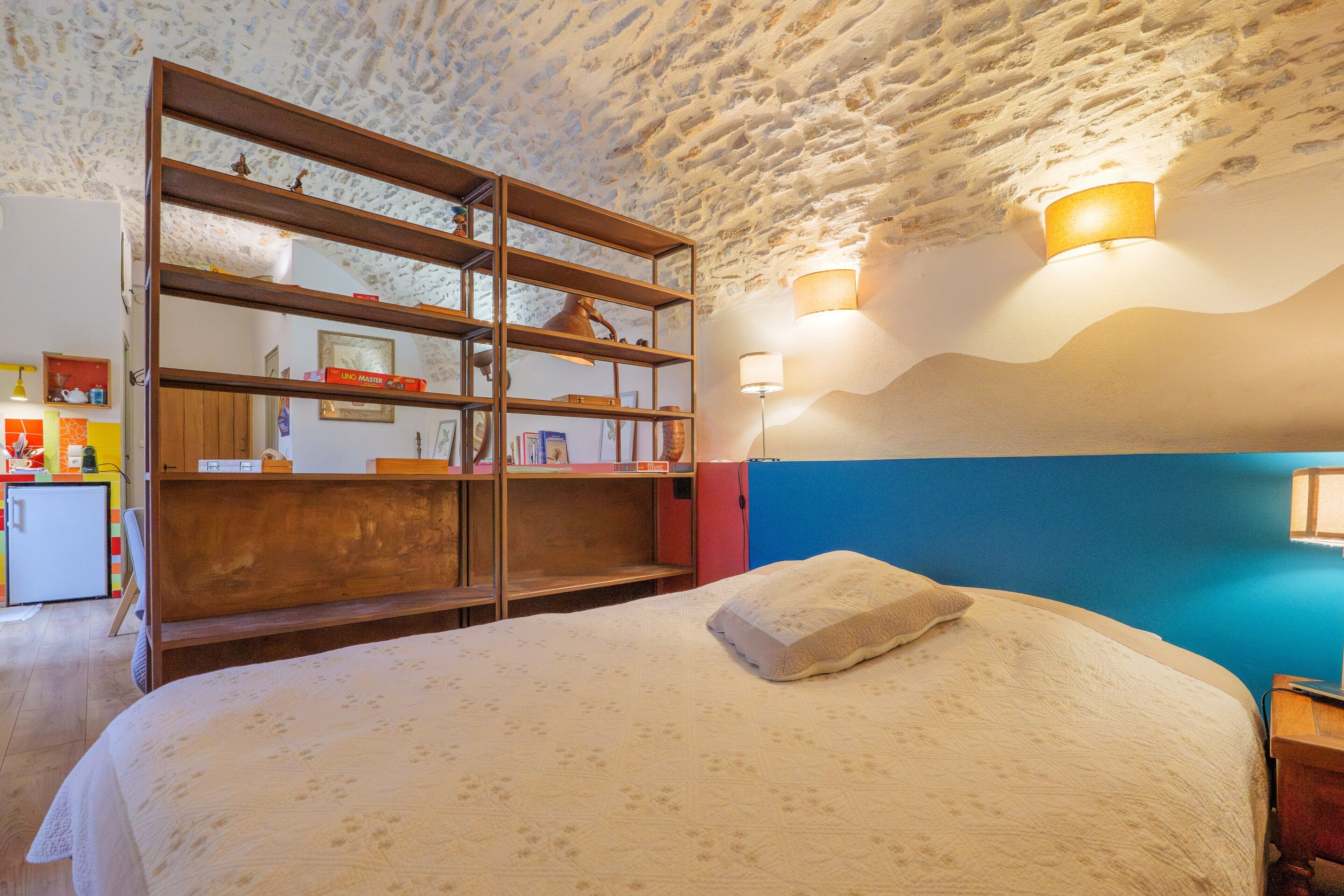Una camera da letto con un letto, una libreria in legno, una lampada a parete e una piccola scrivania con lampada.