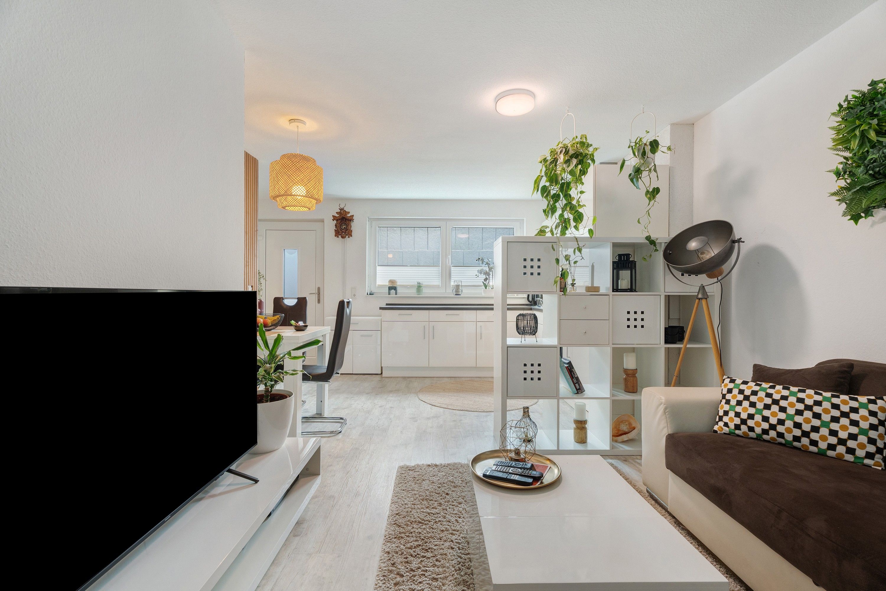 Ein modernes Wohnzimmer mit Flachbildfernseher, einer Couch, einem Couchtisch und einer Küche im Hintergrund.