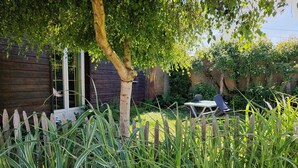 Une maison en bois avec une cour clôturée, une table avec des chaises et de l’herbe haute.