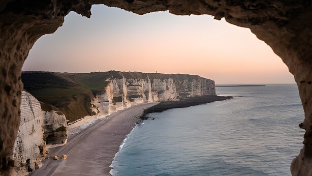 Une vue sur la côte, à travers l’ouverture d’une grotte, avec une plage et des falaises en arrière-plan.