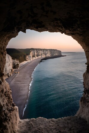 A coastal view through a cave opening, featuring a beach and cliffs. - Cozy Coastal Hideaway Near Fécamp and Étretat (Saint-Léonard)