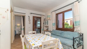 Une pièce avec un lit, une table recouverte d’une nappe à motifs, une fenêtre avec des rideaux et une vue sur la verdure à l’extérieur.