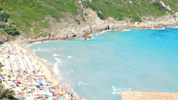 Une plage avec des gens, des parasols et une colline rocheuse.