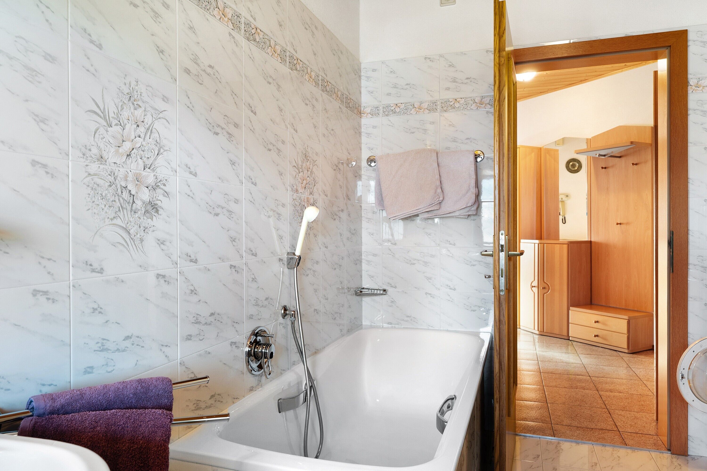 Ein Badezimmer mit einer Badewanne, einer Dusche und einem WC. Ein Handtuchhalter mit Handtüchern und eine Holzkabine mit Schubladen sind ebenfalls vorhanden.