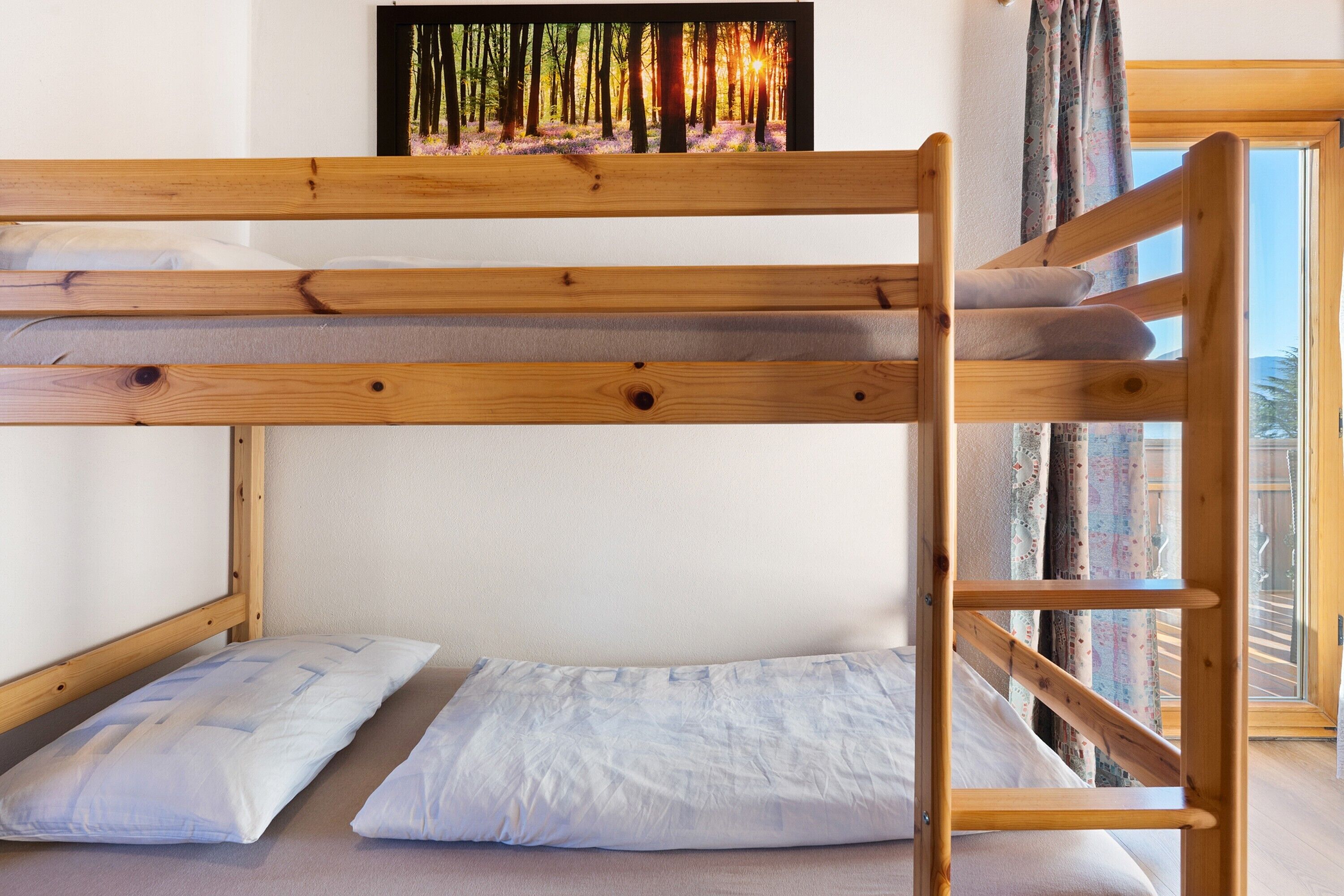 Een stapelbed met houten frame, twee kussens en een lijst met een foto van een bos.