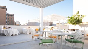 An outdoor patio with white tables and chairs, some with green cushions, and umbrellas.