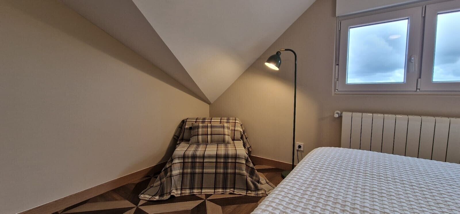 Un dormitorio con cama, lámpara de pie, ventana y radiador.