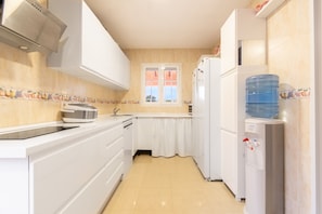 A compact kitchen with white cabinets, a toaster, a sink, a window with curtains, and a water dispenser.