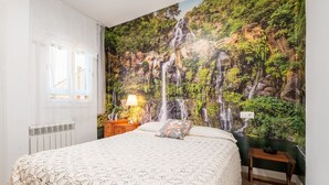 Une chambre à coucher avec un grand lit, une table de chevet, une lampe, une prise électrique fixée au mur et une fenêtre avec des rideaux.