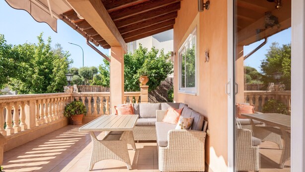Une terrasse couverte, aménagée avec des meubles en osier, une table et des plantes en pot.