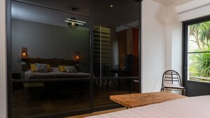 A bedroom with a bed, a wooden table, a chair, a TV, and a sliding glass door leading to a balcony.