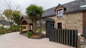 A stone building with a wooden roof, a fenced garden, and a paved walkway.