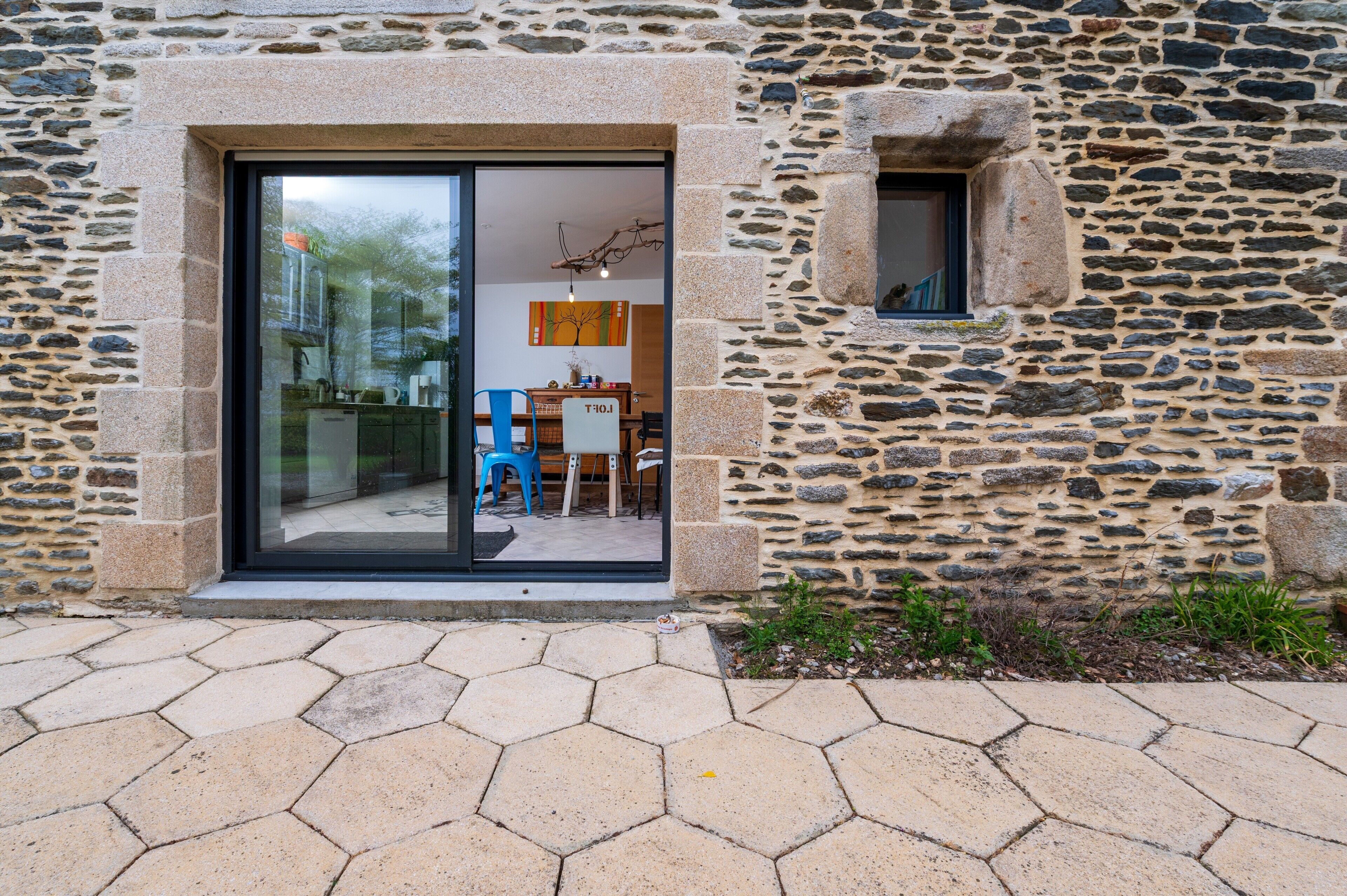 A stone building with a glass door entrance, a small window, and a tiled patio.