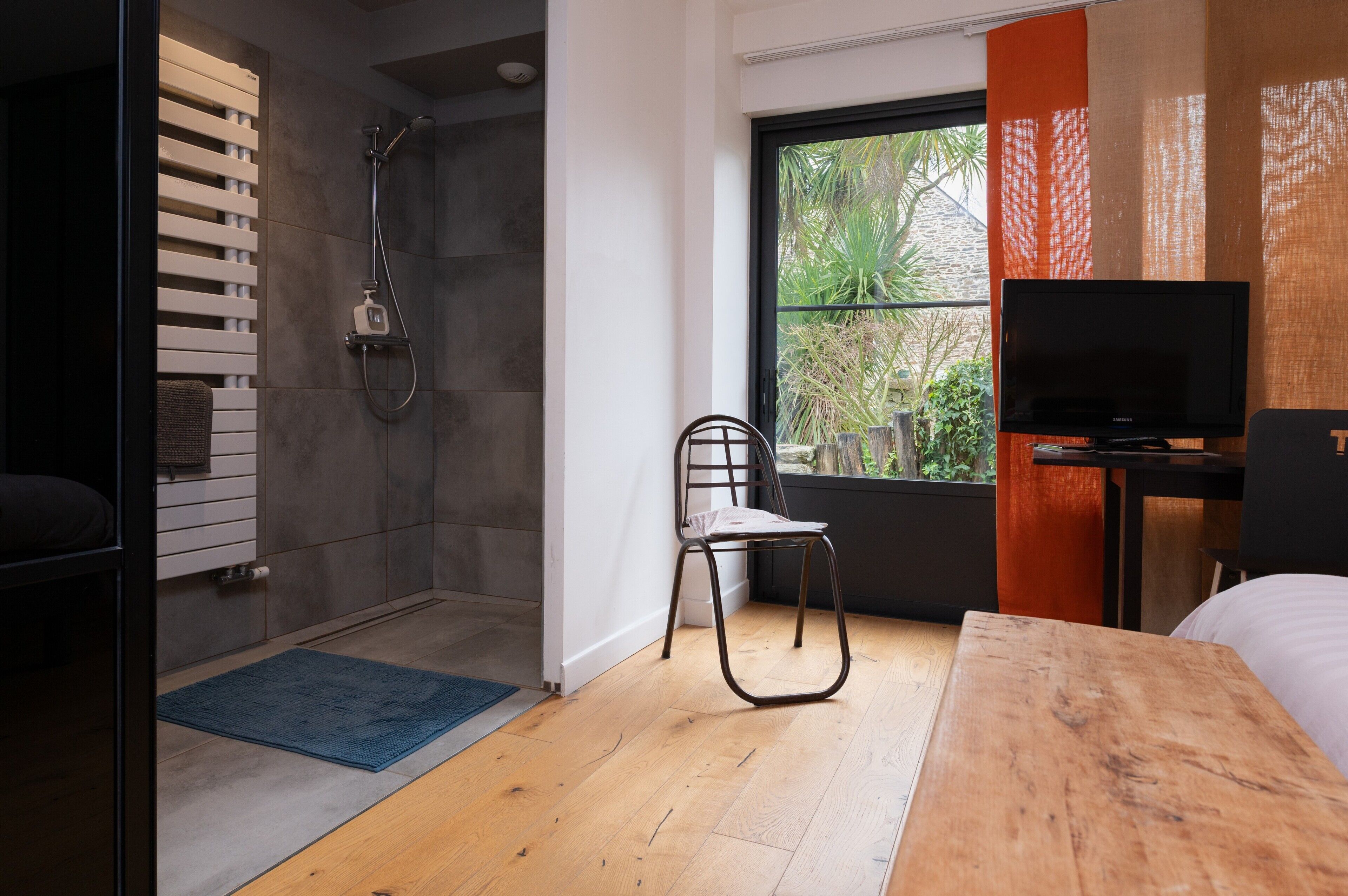 A modern bathroom with a shower, a wooden floor, a chair, and a television.