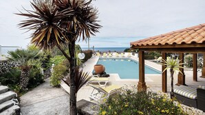 A pool area with lounge chairs, a pergola, and a view of the ocean.