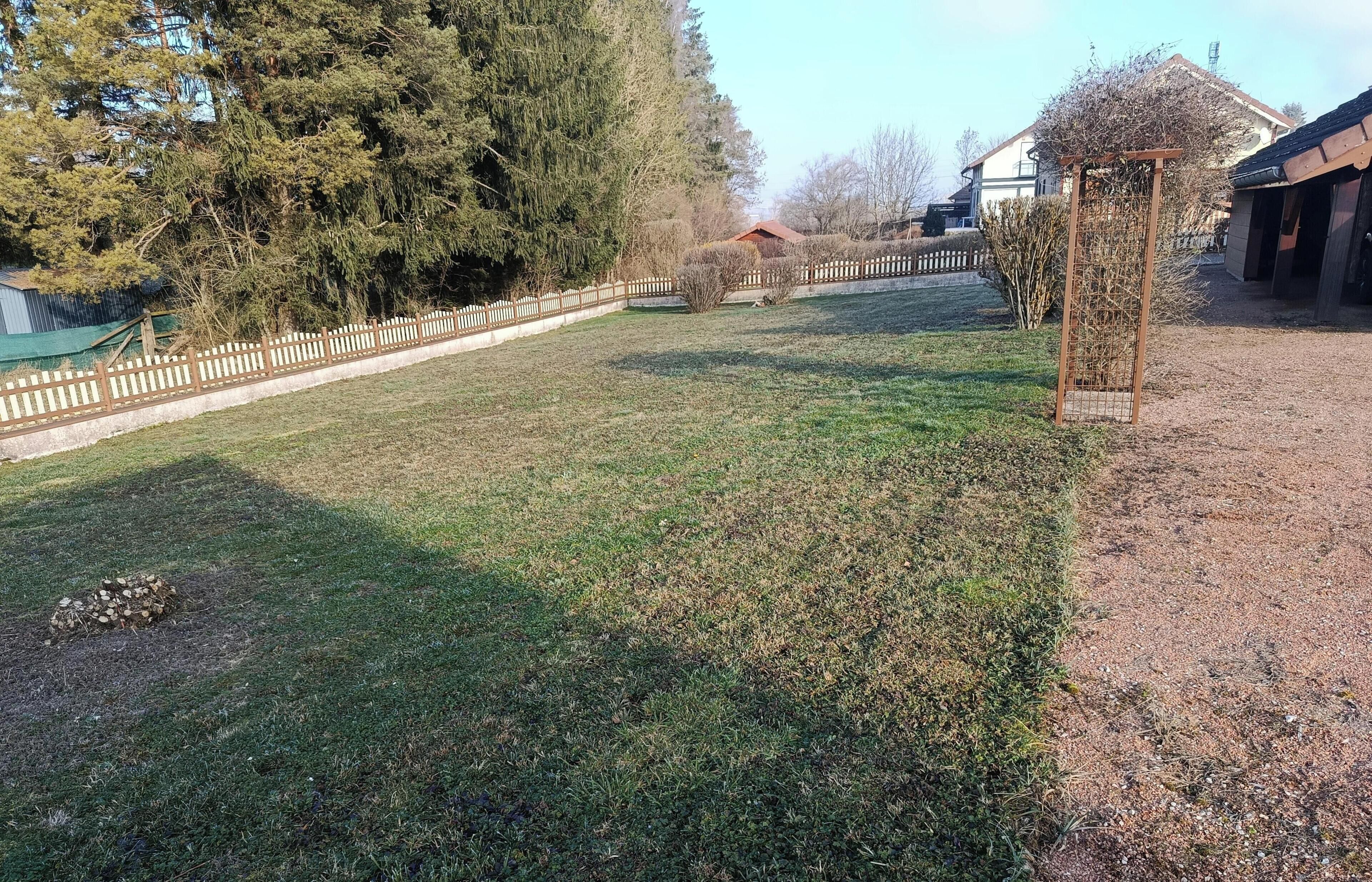 Een gazon met een houten omheining, bomen en een gebouw met een rood dak.
