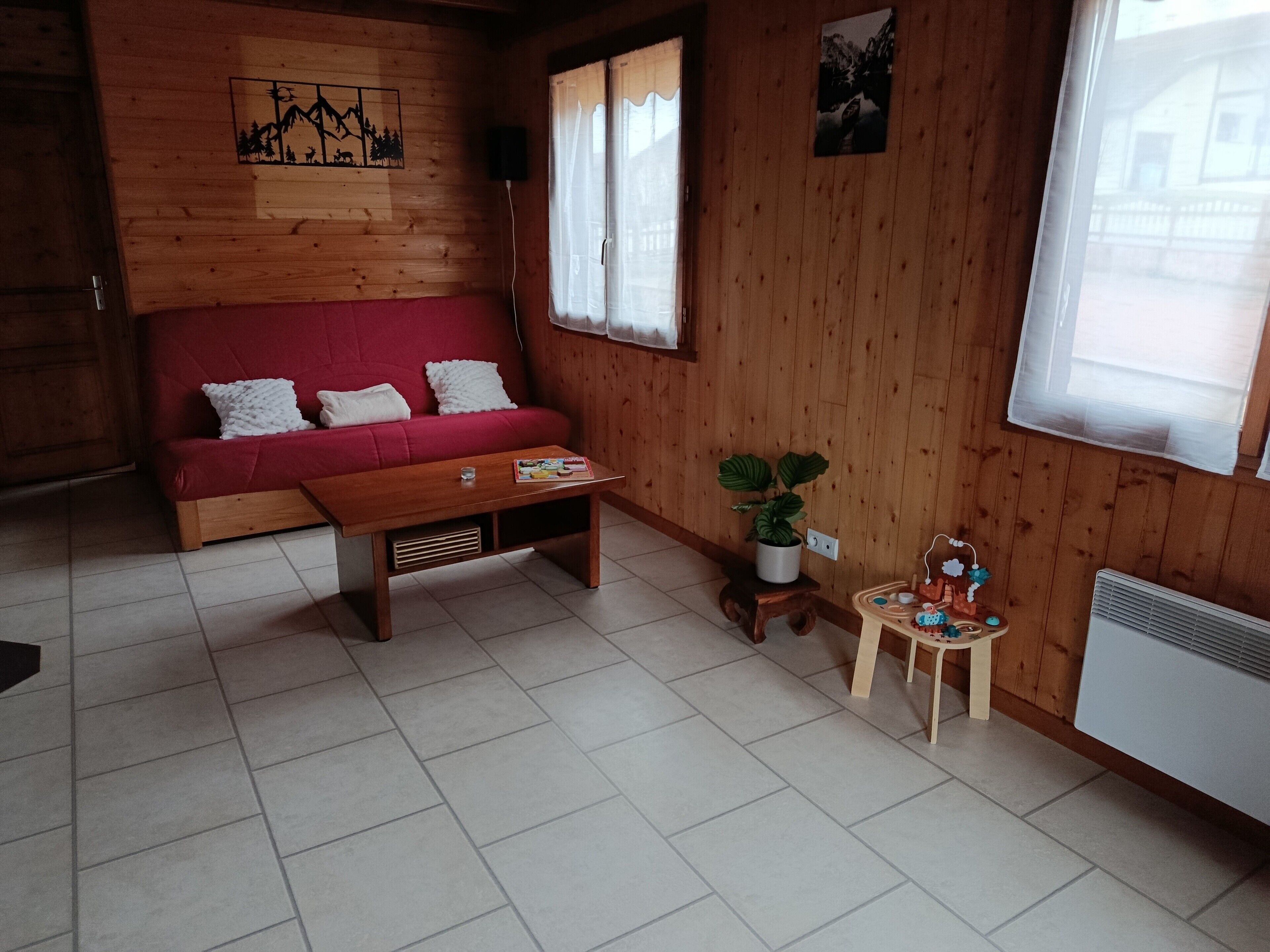 Un interior de madera con un sofá rojo, una mesa de madera, una planta en maceta y un taburete de madera pequeño.