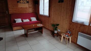 Un interior de madera con un sofá rojo, una mesa de madera, una planta en maceta y un taburete de madera pequeño.