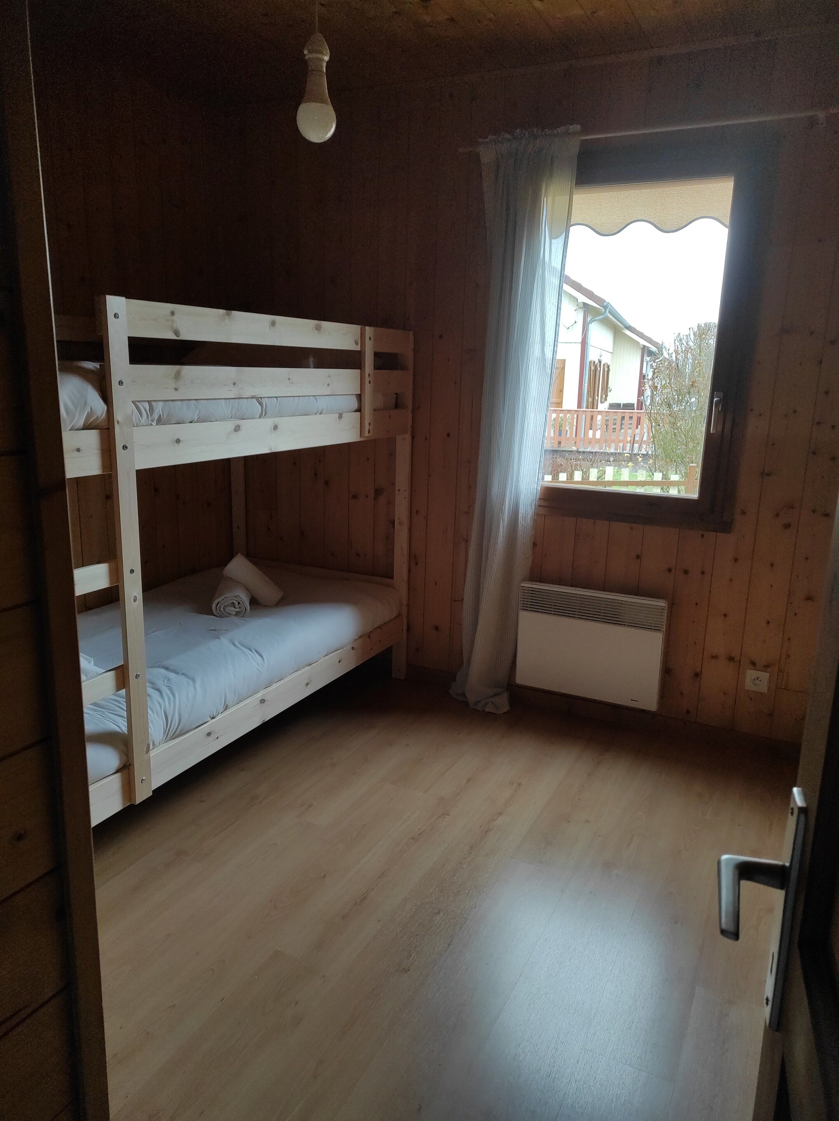 Una camera con un letto a castello, una finestra, pareti in legno e un termosifone.
