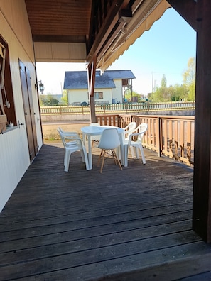 A covered outdoor area with a wooden deck, white plastic chairs, and a table.