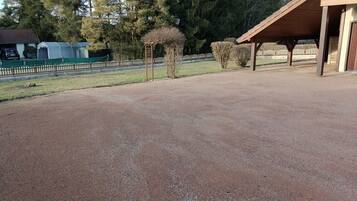 A gravel-covered outdoor area with a covered structure, trees, and a fenced area in the background.
