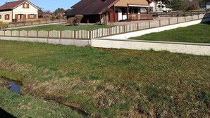 Zona residencial con casas, un patio cercado y un pequeño arroyo.