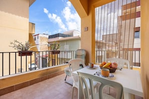 Un balcon avec une table dressée pour deux personnes, un pot de fleurs et une vue sur les bâtiments voisins.