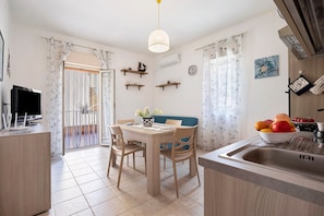 Une cuisine compacte comprenant une table à manger, des chaises, un luminaire suspendu et un évier.