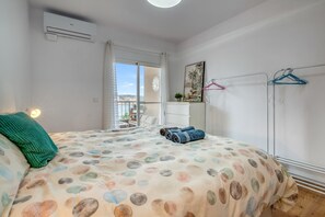 A bedroom with a bed, an air conditioner, a window with a view, and a clothing rack.