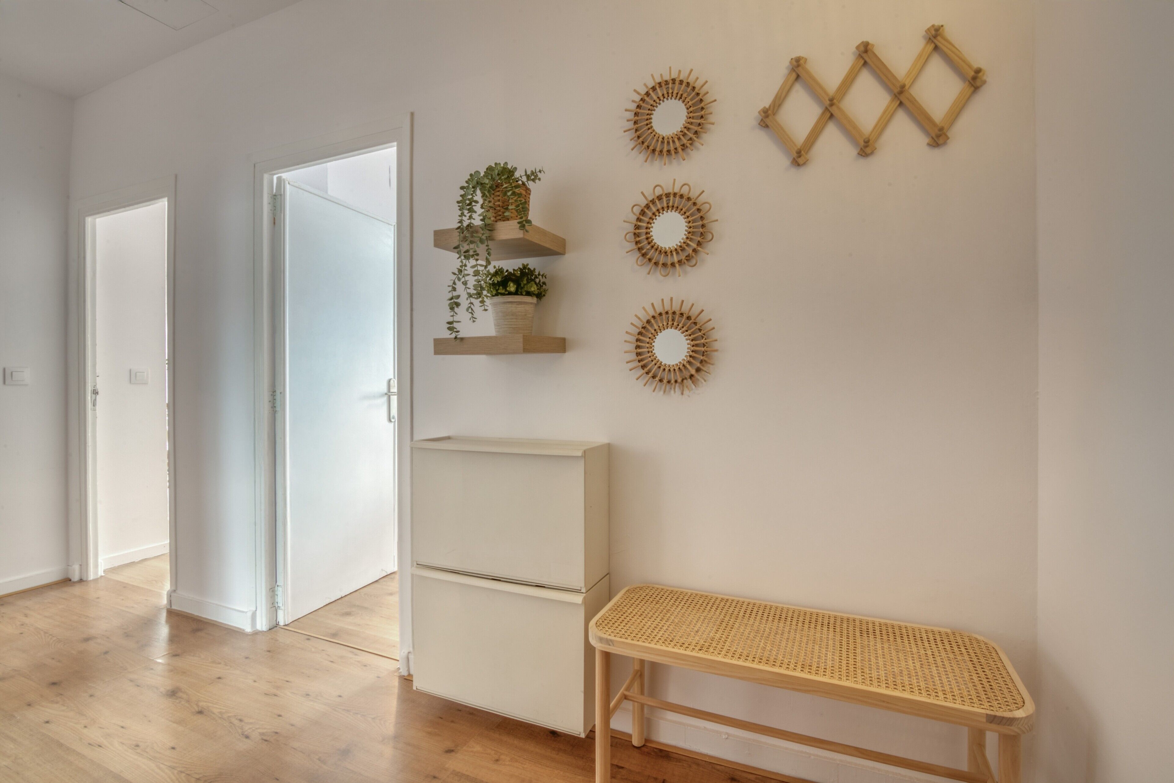 A room with a wooden floor, a white wall, a white bench, and decorative wall art.
