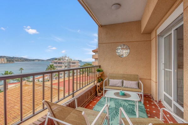 A balcony with a view of the sea, a small table, a sofa, and a decorative wall plate.