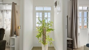 A room with a large potted bamboo plant, white walls, a wooden floor, and a window with curtains.