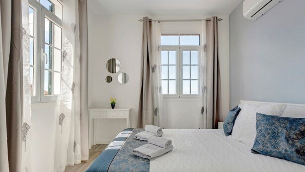 A bedroom with a bed, a bedside table, a mirror, and a window with curtains.