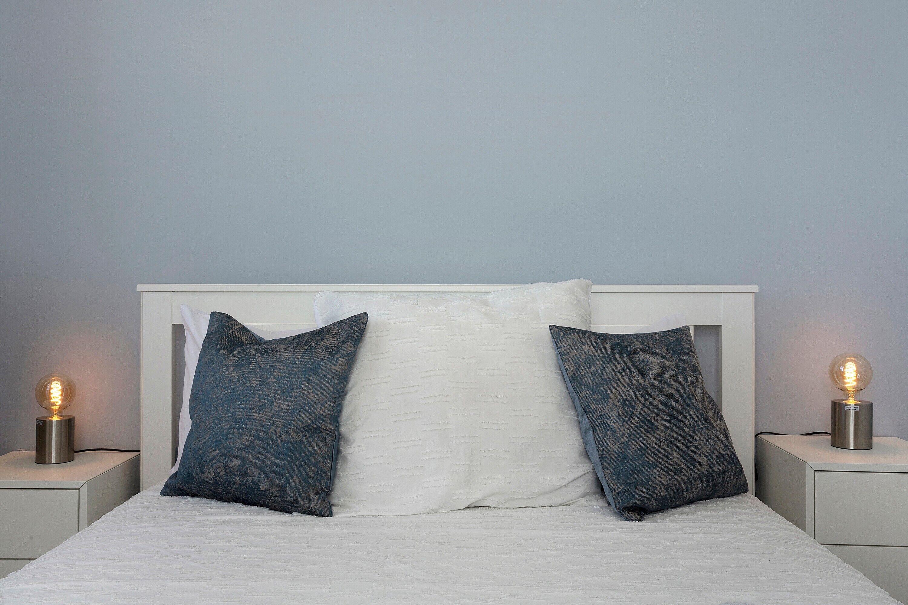A bed with white bedding, two dark patterned pillows, and two bedside lamps on nightstands.