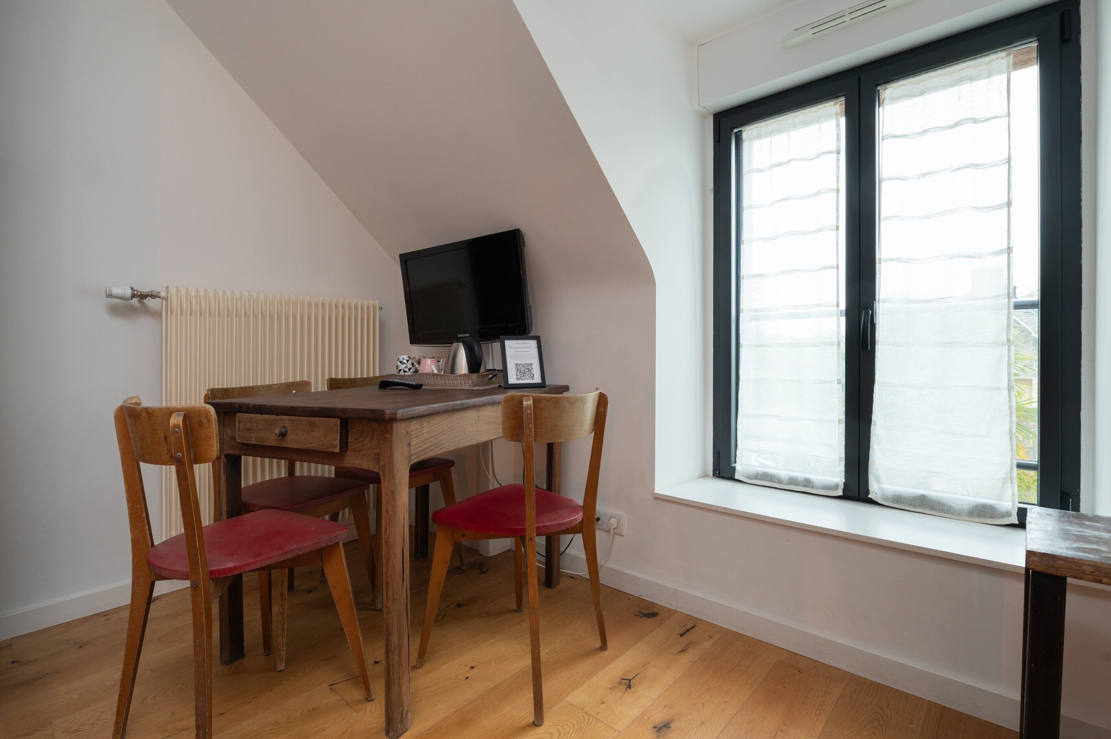 A room with a wooden desk, two chairs, a television, and a window with blinds.