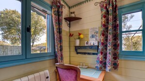 Une pièce avec une fenêtre, un radiateur, une table avec une chaise et une étagère ornée d’objets décoratifs.