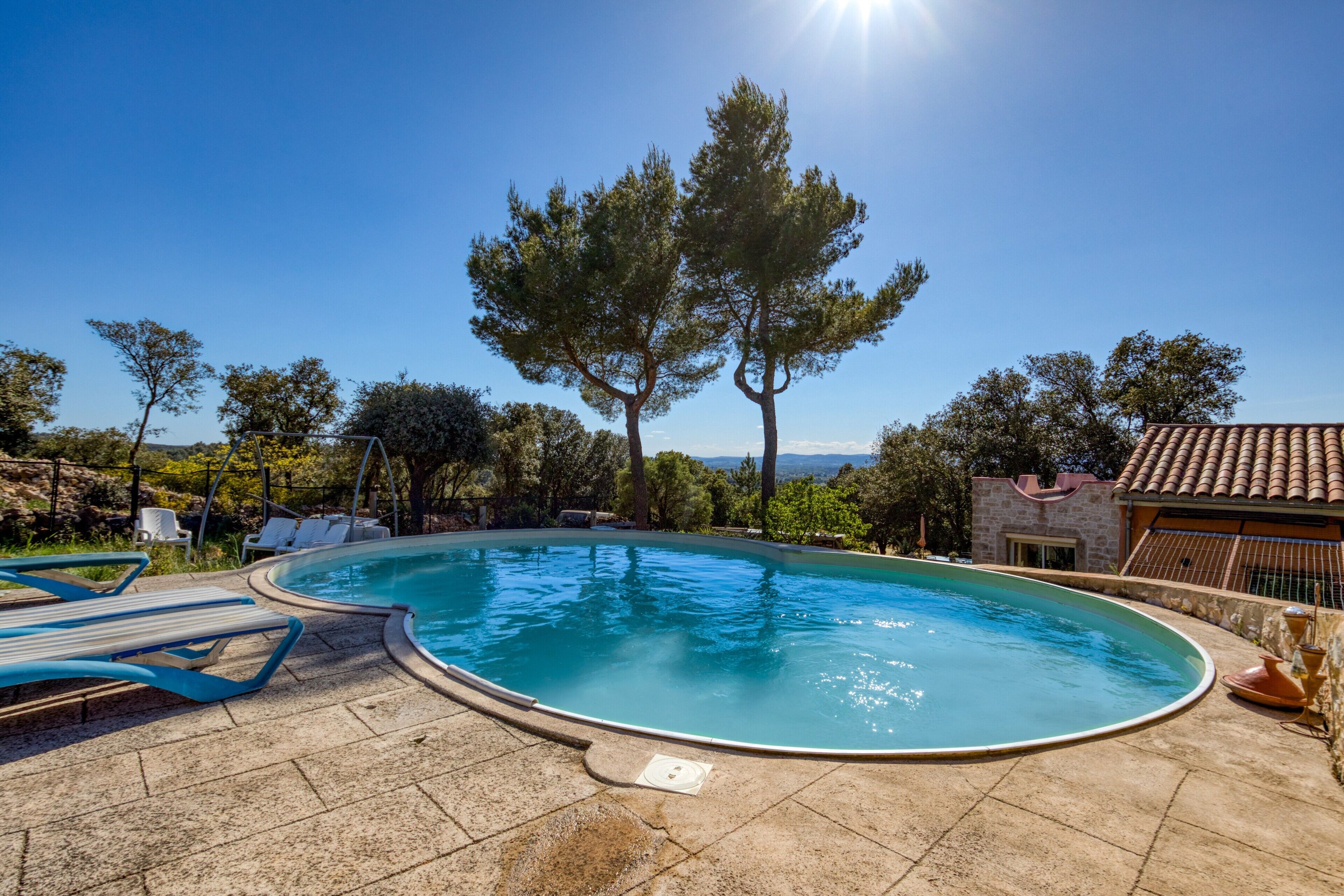 A swimming pool with lounge chairs, surrounded by trees and a stone building.