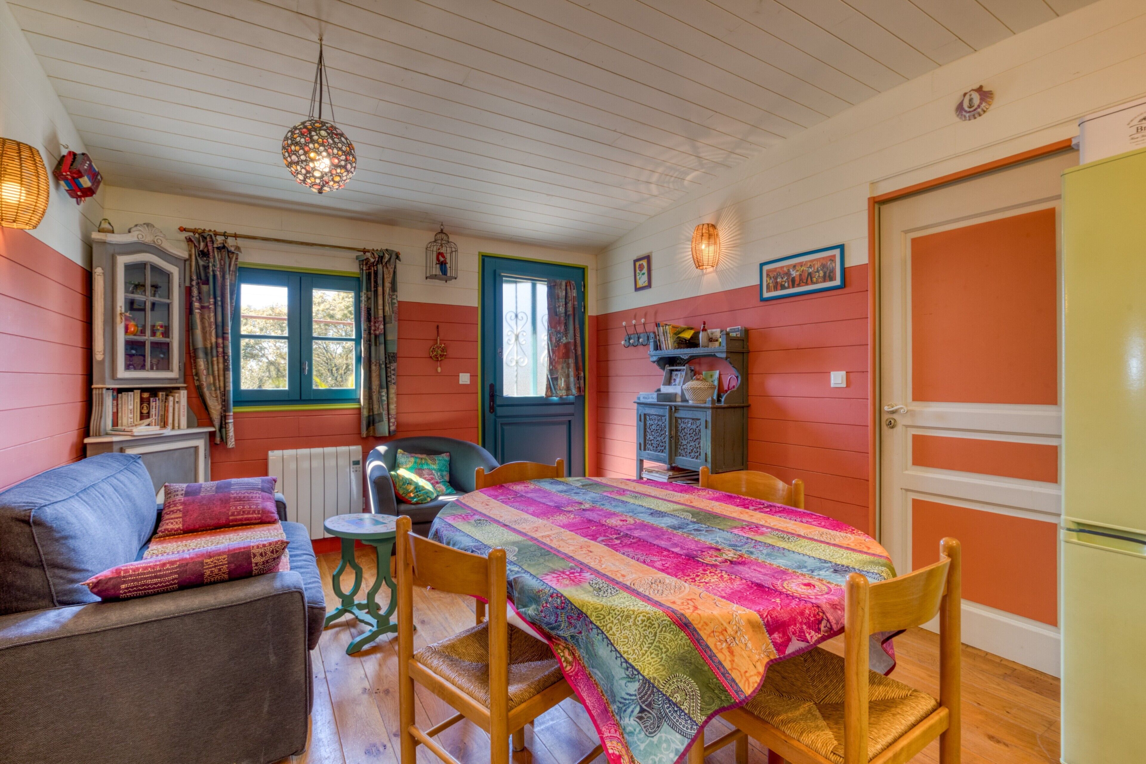 A cozy room with a wooden floor, a colorful quilted tablecloth, a sofa, a chair, a cabinet, and a door.