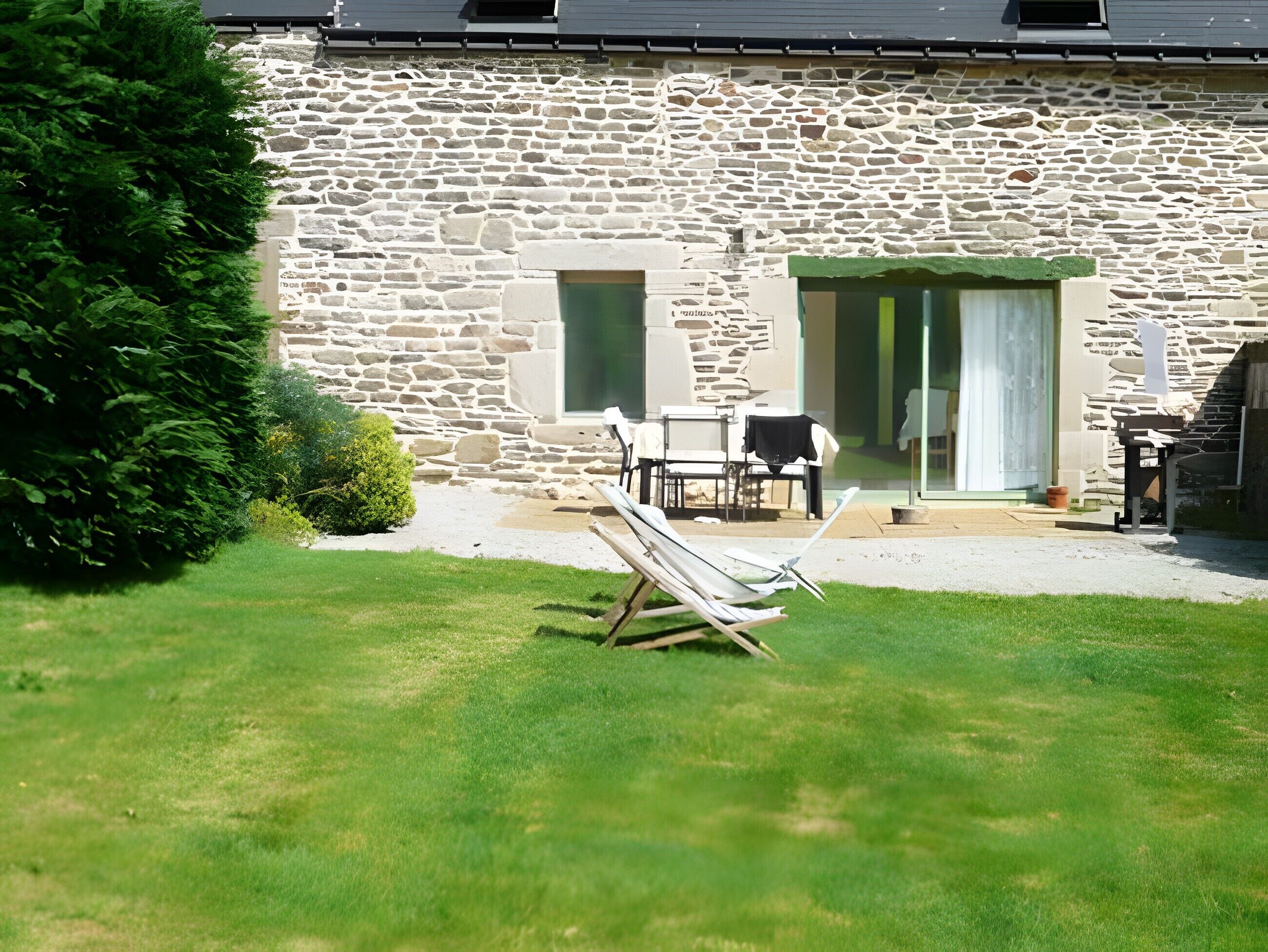 A stone building with a patio, a lawn, and a bench.